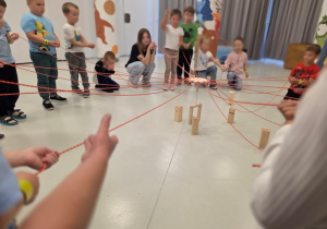 Dzieci uczestniczą w zespołowej grze integracyjnej ze sznurkami i klockami.